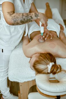 professional female specialist is doing cupping therapy on the back of beautiful caucasian lady