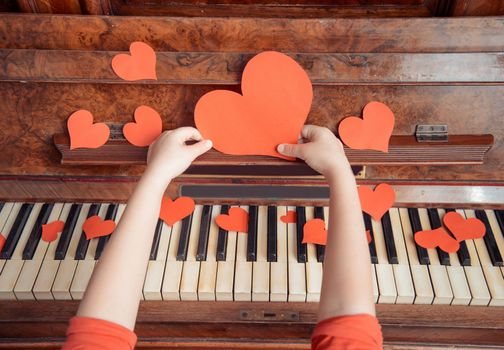 Unrecognizable child holds red paper heart on a background of piano, close-up