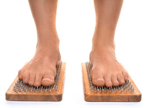 Front view of a male feet stand on a board with sharp nails over white background. Sadhu's board - practice yoga. Pain, trials, health, relaxation, cognition. Close-up.