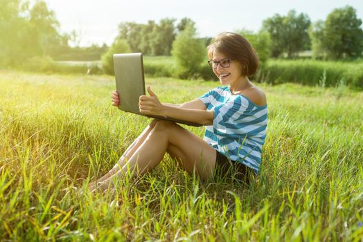 A smiling woman rests in nature and talks on video call