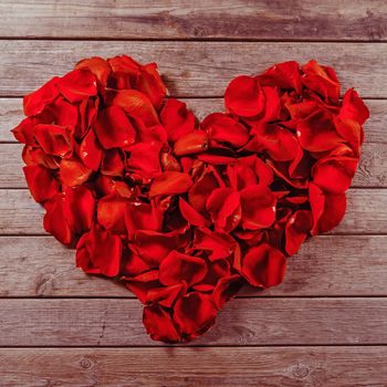 Rose red petals in the shape of heart on a wooden table