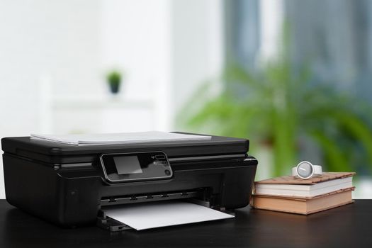 Stack of books and home printer against blurred background, close up