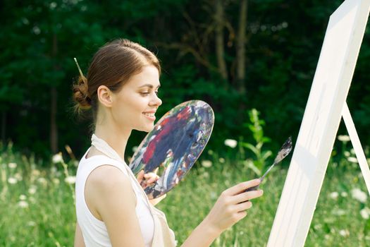 woman artist outdoors with palette of paints paints a picture. High quality photo