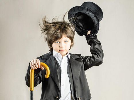 Young six year old boy wearing black suit expressively taking off his top hat. Retro party costume, Illusionist performance