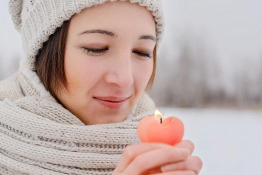 Young woman holds a candle in the shape of a heart in winter