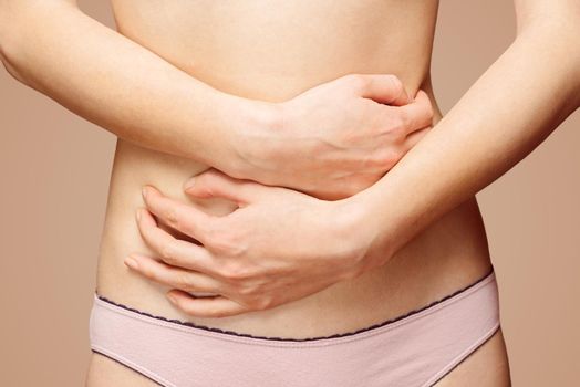 Unrecognizable woman holds her abdomen, front view, abdominal or menstrual pain
