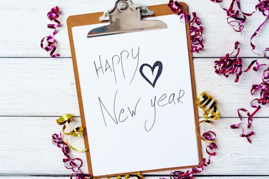 Clipboard with blank sheet of paper and party streamers on white wooden table, top view
