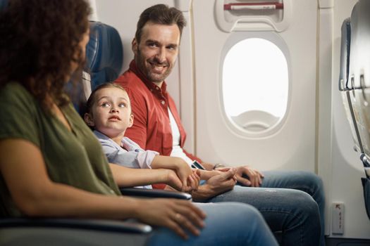 Cheerful caucasian family parents with little daughter holding hands together while sitting on the airplane. Transportation concept