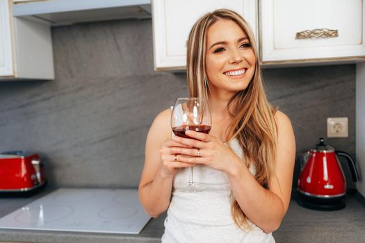 Attractive young woman relaxing with wineglass at her kitchen at home