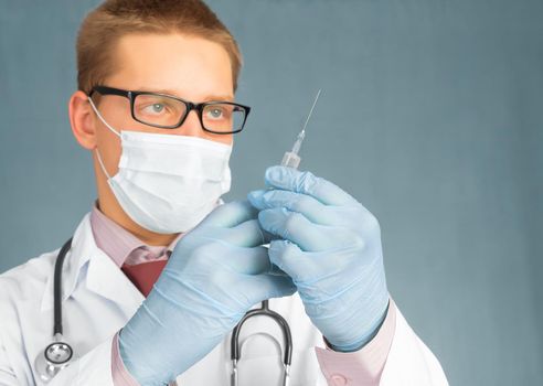 Man doctor in mask and gloves holds a syringe