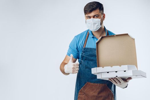 Pizza delivery man in medical gloves and mask against grey background. Safe service while coronavirus covid-19 outbreak