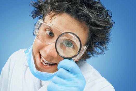 Crazy happy scientist looks through a magnifying glass on a blue background