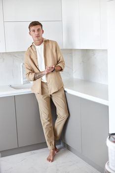 Happy handsome man is standing on minimalistic kitchen and smiling