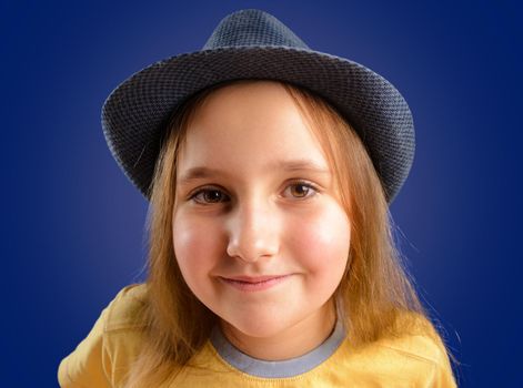 Portrait of happy little girl in a hat on a blue background