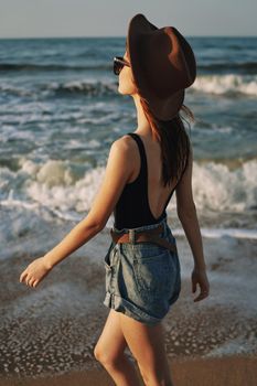 cheerful woman in sunglasses and a hat walks along the ocean. High quality photo