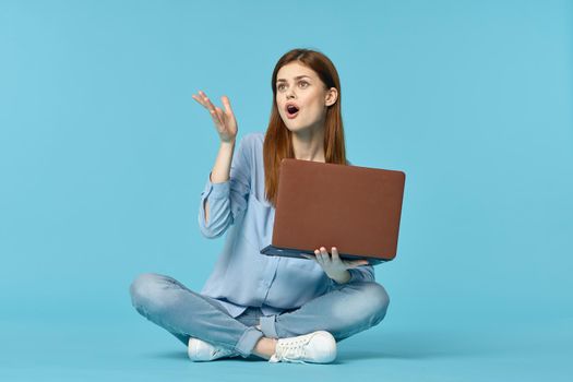 woman with laptop sitting on the floor learning student technology blue background. High quality photo