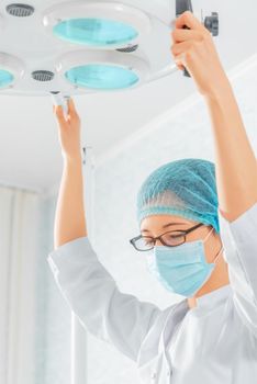 Nurse in a mask and cap places a surgical lamp for operation