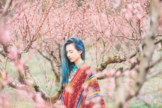 Boho style young woman walking in pink flowering peach tree garden
