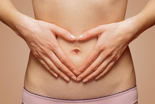 Unrecognizable woman holds her hands in heart shape in front of her abdomen