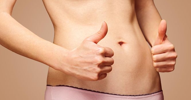 Woman with gesture sign thumb up in front of her slim abdomen