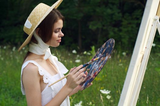 woman with a palette of paints painting a picture outdoors close-up. High quality photo