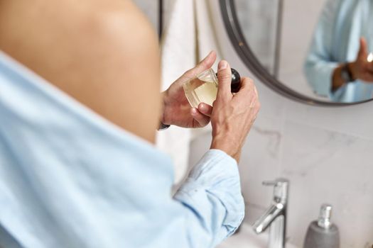 Photo of adult caucasian beautiful man in front of mirror in light modern bathroom