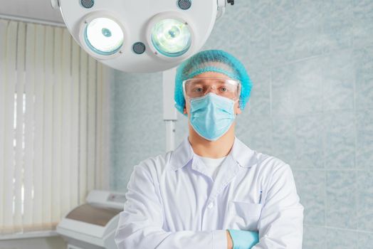 Man doctor surgeon in a mask and cap stands in an operating room