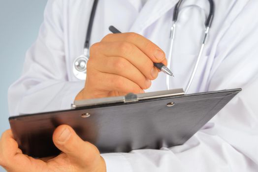 Unrecognizable doctor writes medical records on clipboard
