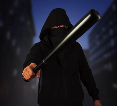 Dangerous man in the mask with baseball bat ready for fight in the night city