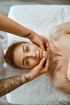 Therapist is doing face relaxing massage to a young woman in modern wellness cabinet