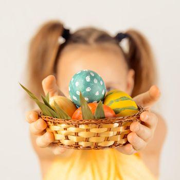 Little girl gives Easter basket with colored eggs, focus on eggs