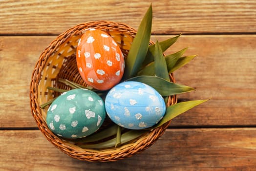 Basket with colored eggs on a wooden table, top view, copyspace