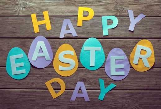 Inscription Happy Easter day on paper eggs on a wooden table