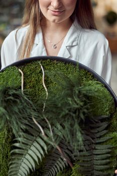 Confident female florist is holding a plant composition in her own flower and plants shop