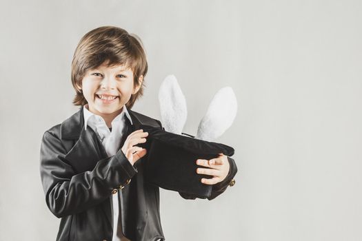 Adorable child dressed as an illusionist getting bunny from a hat over grey background