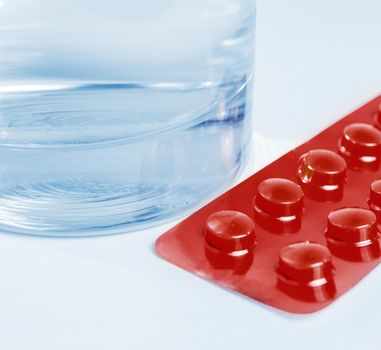 Glass of water and blister of drugs on white background