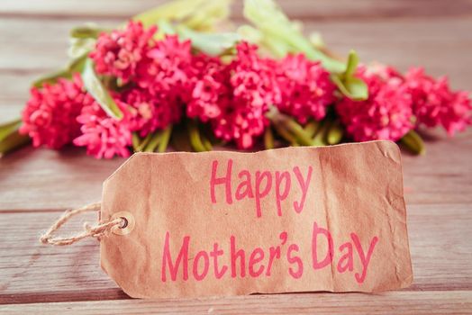 Red hyacinths and a card with text Happy Mother’s Day on a wooden table