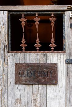 closeup the word GUEST ONLY painted on old rusty steel on old wooden door