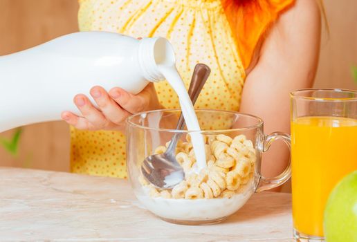Little girl pours milk in cereal flakes for breakfast, face is not visible
