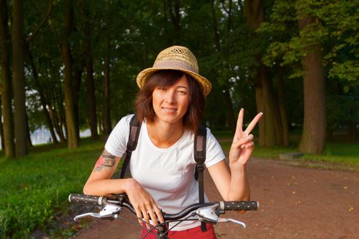 Hipster girl doing victory sign while sitting on a bicycle