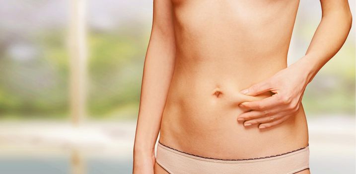 Woman holds a fold of skin on the abdomen in swimming pool