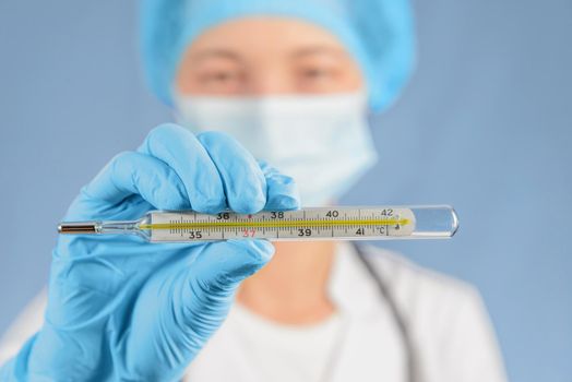 Woman nurse in a cap and mask holds thermometer, focus on thermometer