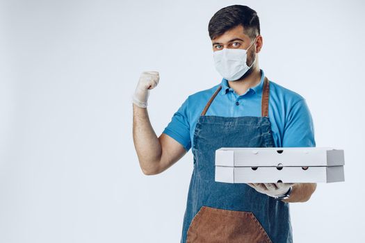 Pizza delivery man in medical gloves and mask against grey background. Safe service while coronavirus covid-19 outbreak