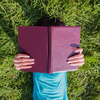 Girl lying in a meadow, holding aloft a book