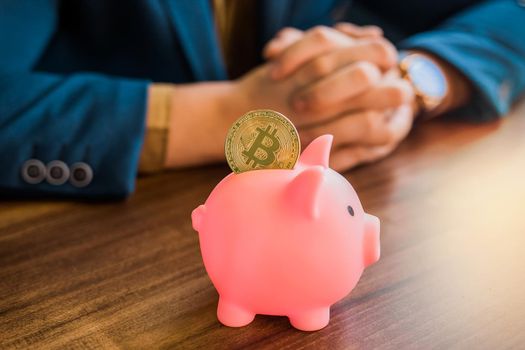Golden bitcoin cryptocurrency in a pig piggy bank on the table on the background of a businessman. Bitcoin and cryptocurrency concept.