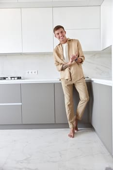 Happy handsome man is standing on minimalistic kitchen and smiling