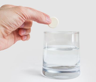 Man's hand throws a medical tablet in a glass with water