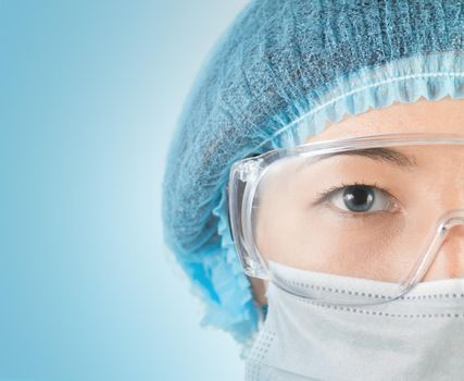 Young woman surgeon in cap, glasses and mask looks at camera, close-up