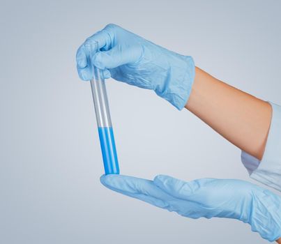 Human hands in gloves holding a test tube with blue liquid
