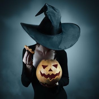 Woman in witch costume opens carved Halloween pumpkin